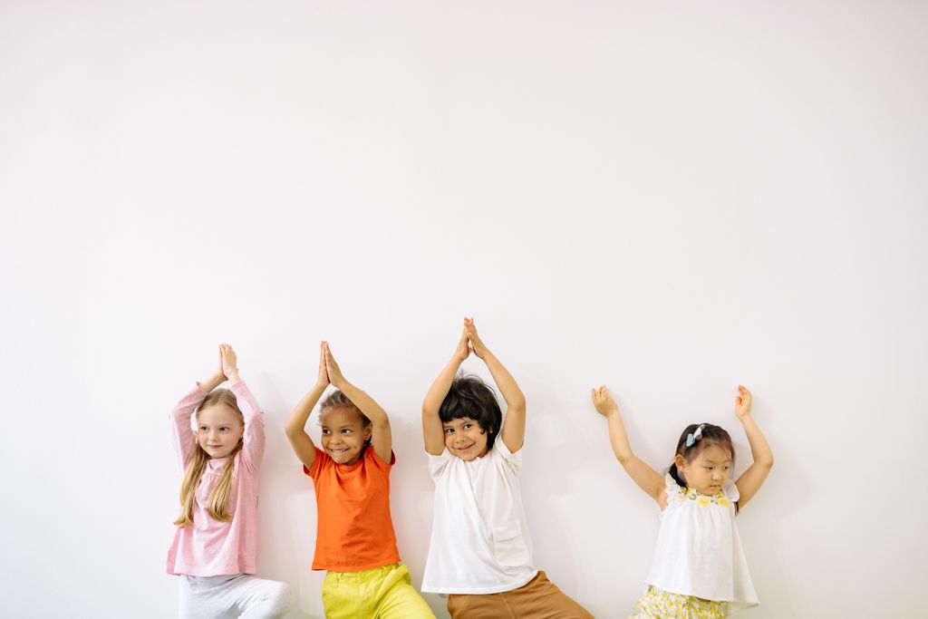 Four diverse children joyfully doing yoga poses in a bright room, showcasing fun and fitness.